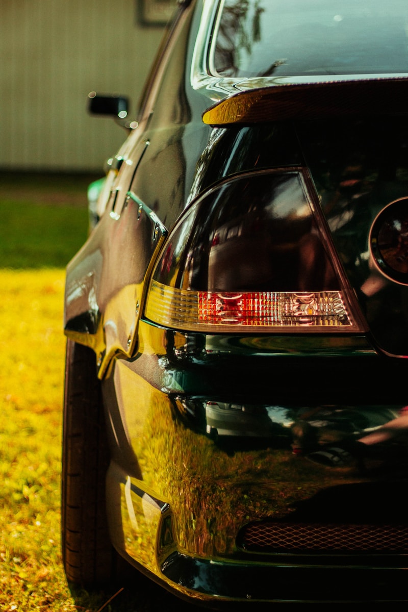 Here's a caption: black car's taillight shines in the sunlight.